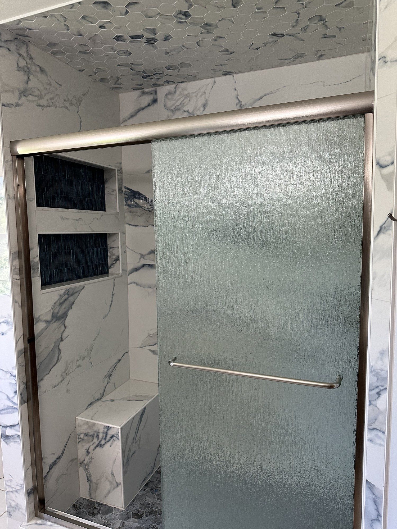 Walk-in shower with frosted glass door and marble-look tile