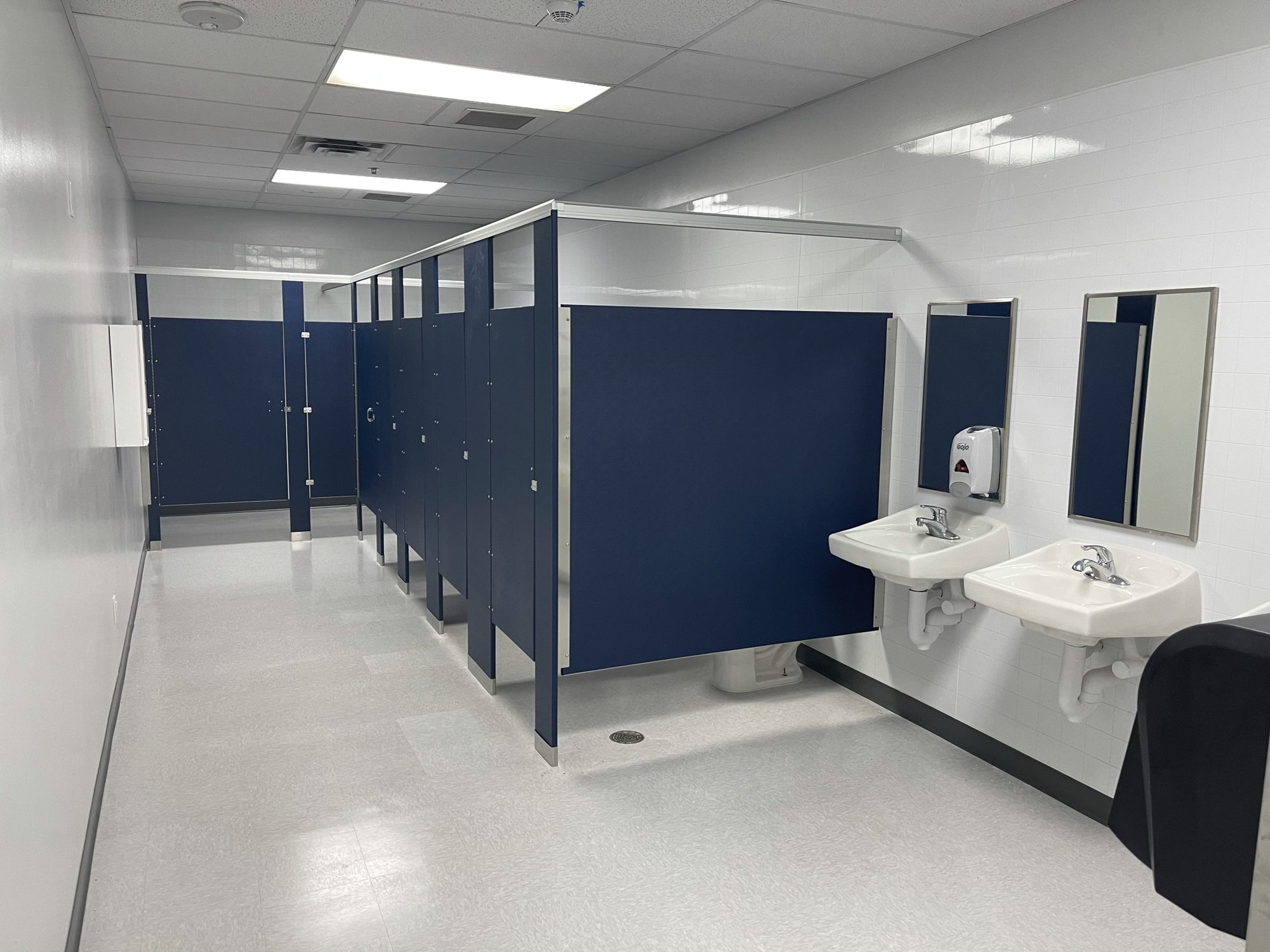 Commercial restroom with navy partitions, wall-mounted sinks, and light flooring