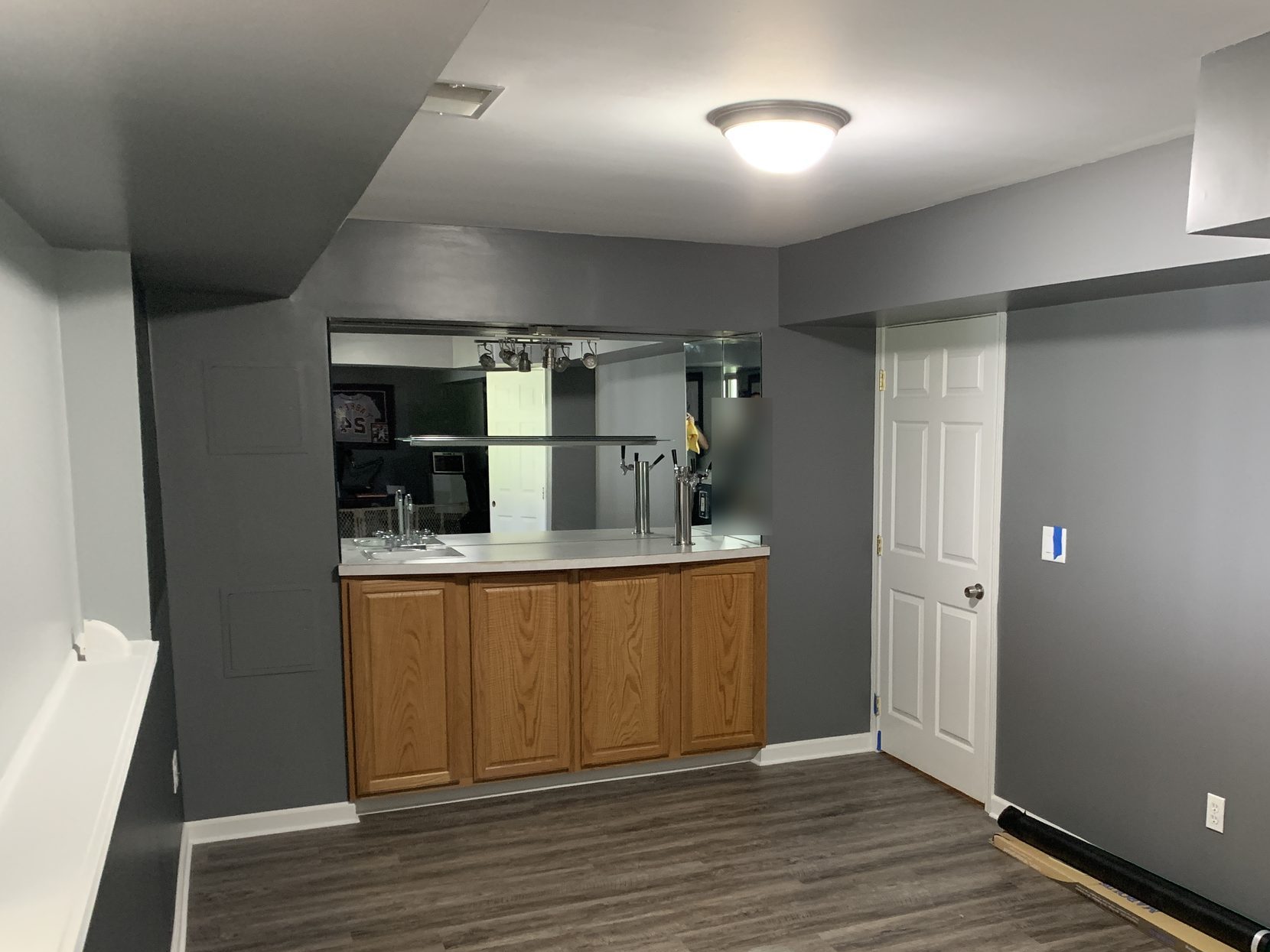 Finished basement bar area with gray LVT flooring, oak cabinets, and fresh gray paint