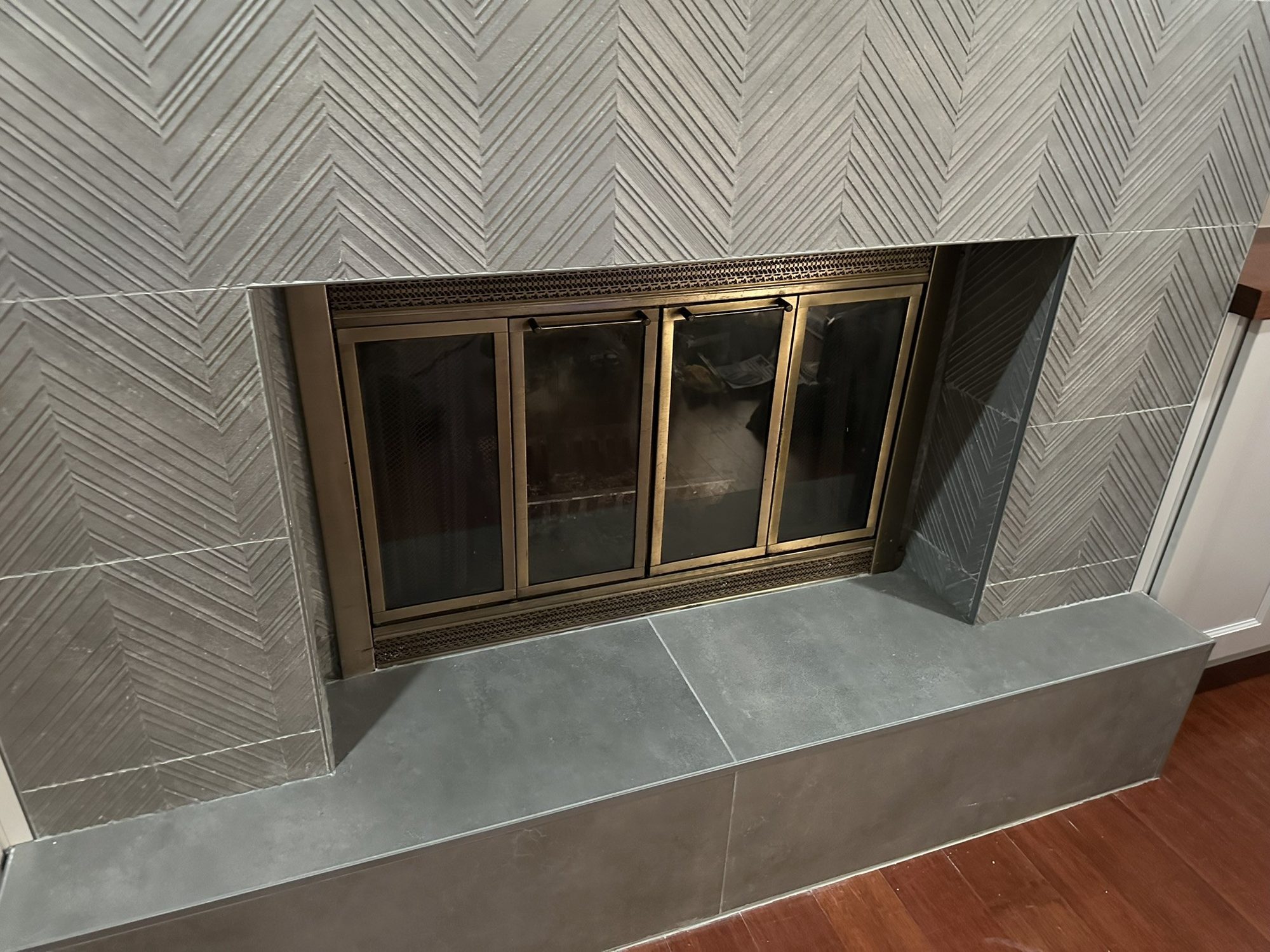Fireplace with herringbone tile surround and brass-framed glass doors